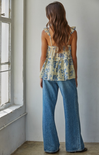 Woman wearing a floral top and blue jeans standing in a room with a window.