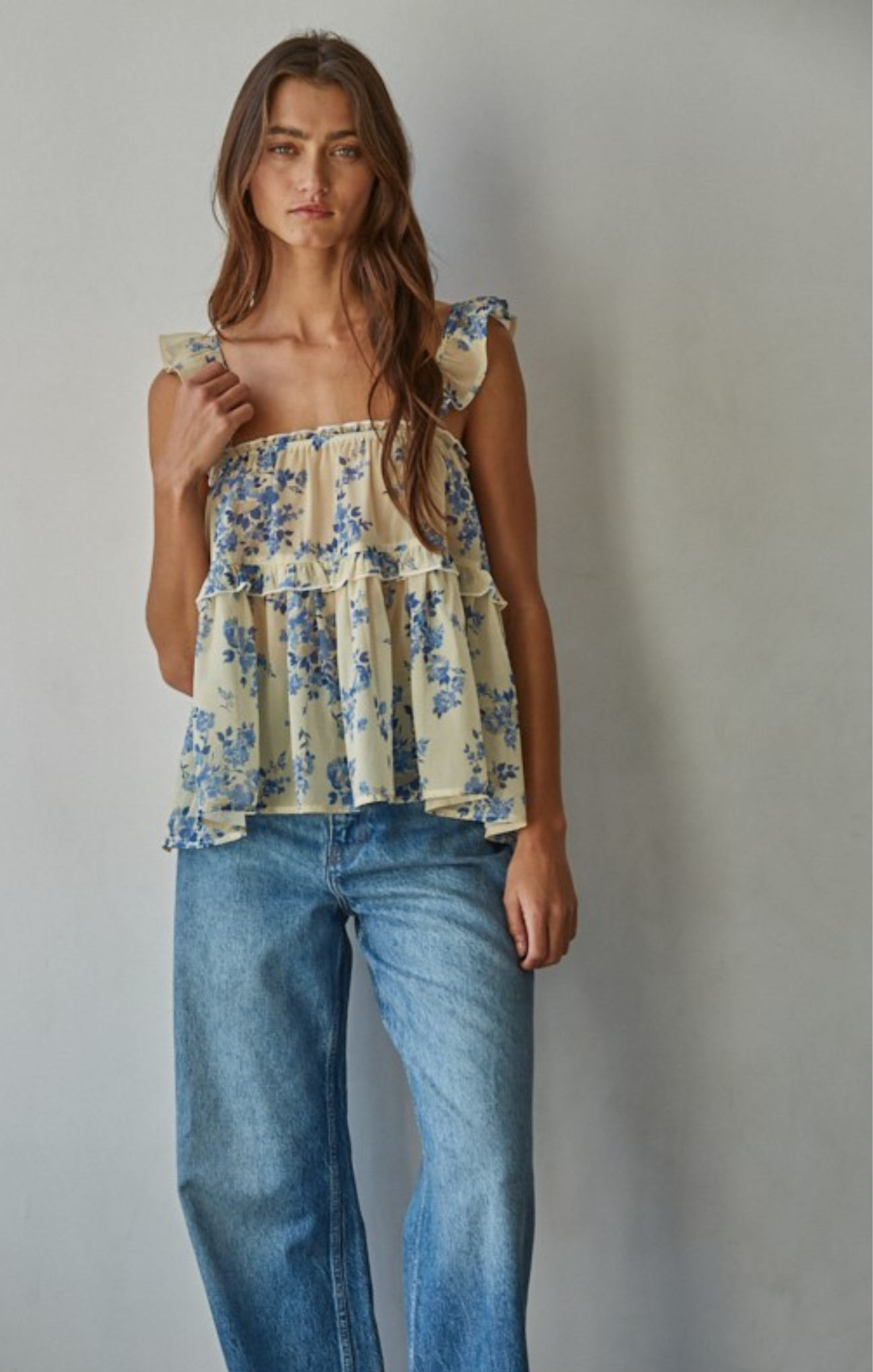 Woman wearing a floral top and blue jeans against a plain background