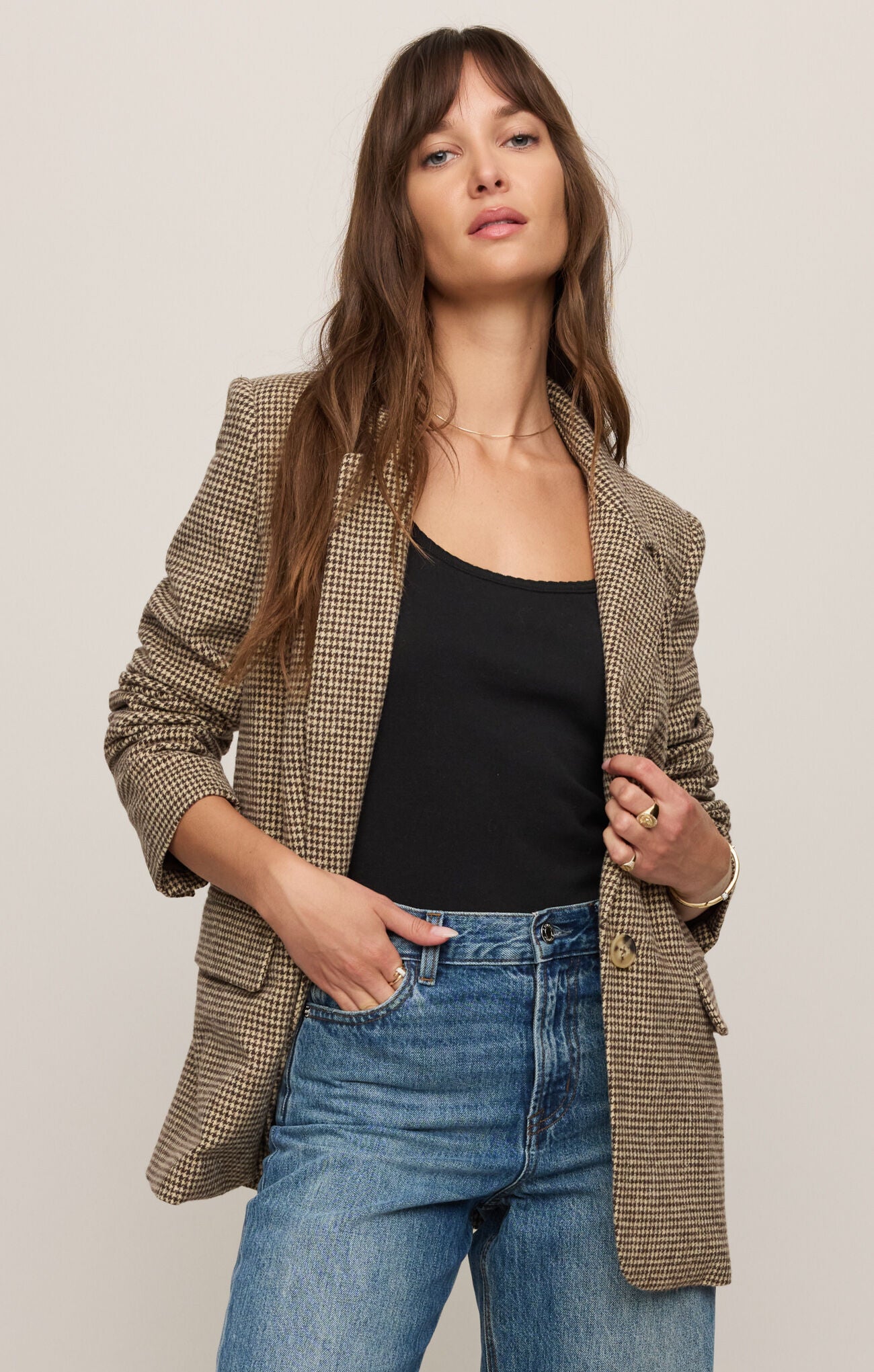 Woman wearing a plaid blazer over a black top and blue jeans on a plain background