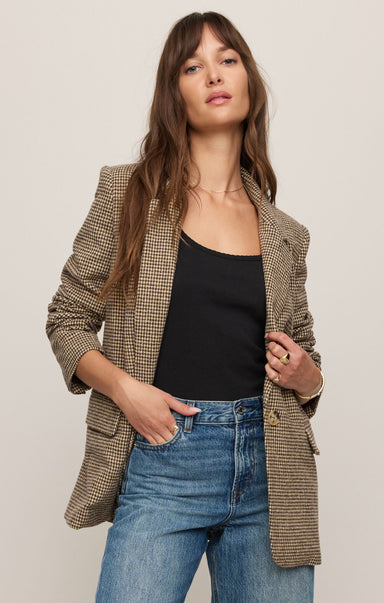 Woman wearing a plaid blazer over a black top and blue jeans on a plain background