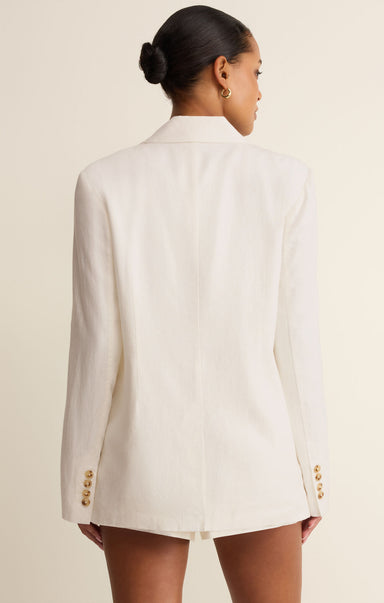 Woman wearing a white blazer with gold buttons on a beige background