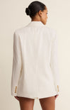 Woman wearing a white blazer with gold buttons on a beige background