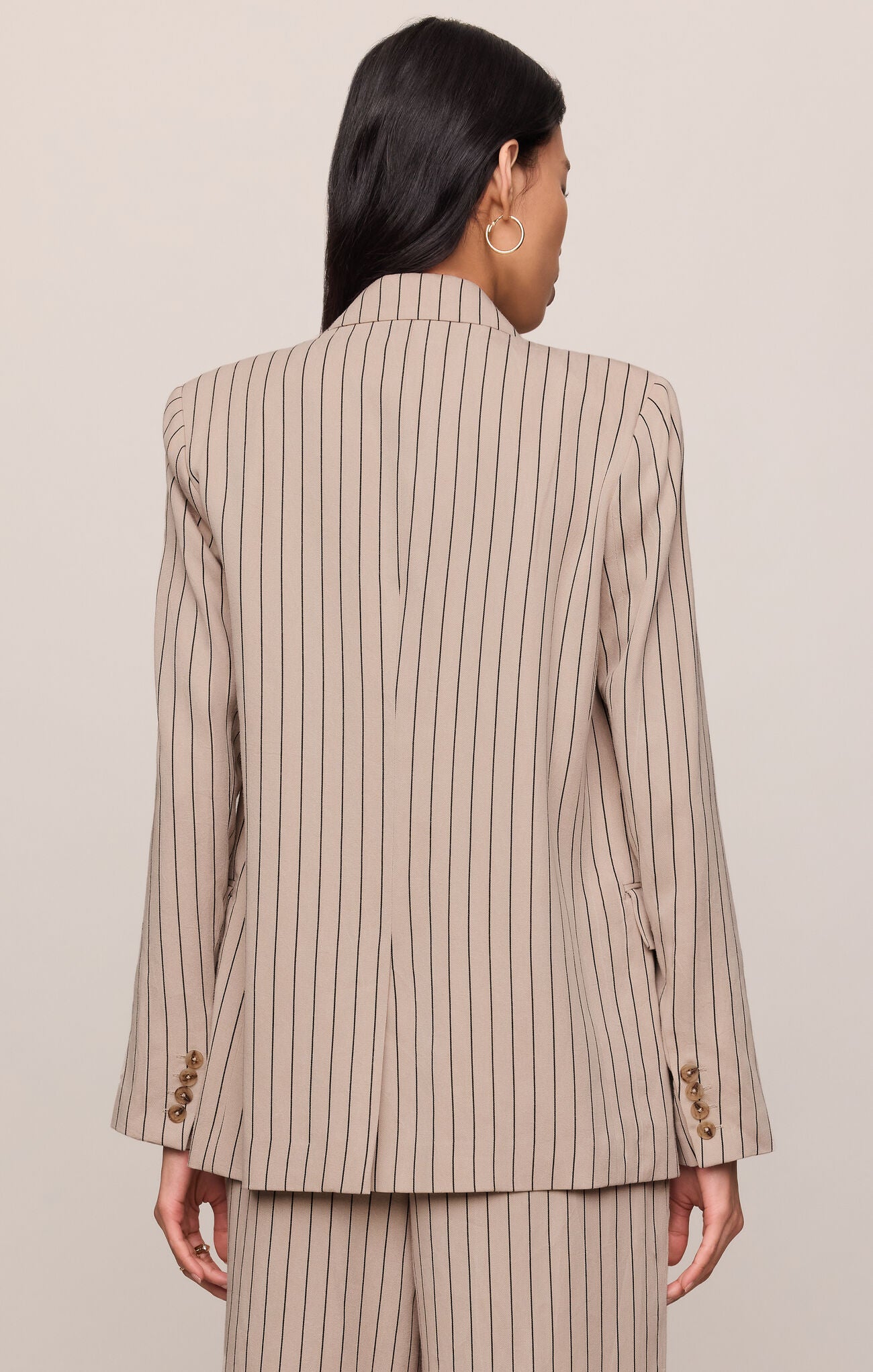 Person wearing a beige pinstripe suit against a plain background