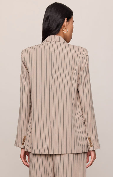 Person wearing a beige pinstripe suit against a plain background