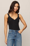 Woman wearing a black tank top with lace details and blue jeans against a beige background