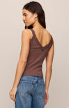 Woman wearing a brown tank top with lace details and blue jeans on a beige background
