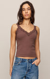 Woman wearing a brown tank top with lace details and blue jeans against a beige background