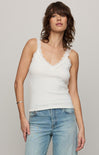 Woman wearing a white lace-trimmed tank top and blue jeans against a plain background