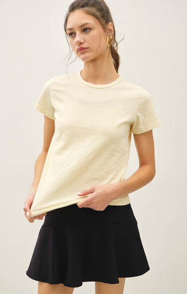 Woman wearing a light yellow t-shirt and black skirt on a plain background