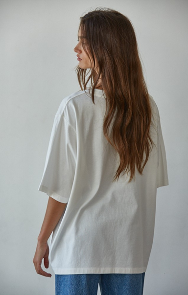 Person wearing an oversized white shirt and blue jeans against a plain background