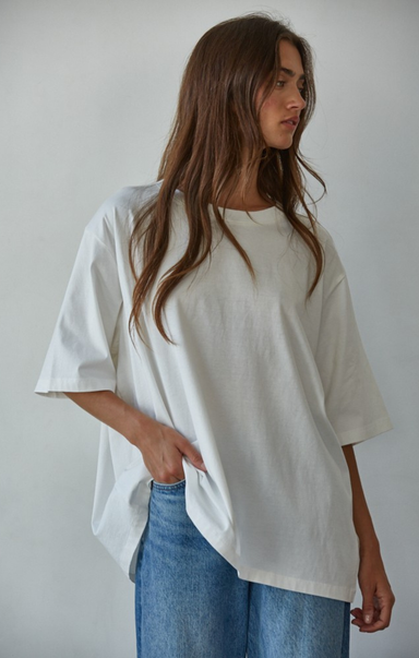 Woman wearing an oversized white t-shirt and blue jeans against a plain background