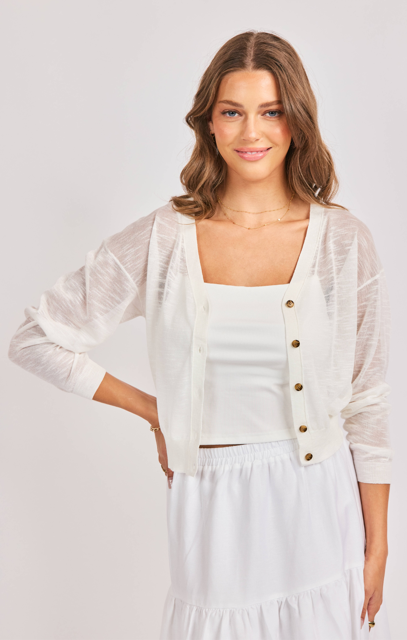 Woman wearing a white outfit with a sheer cardigan on a plain background