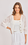 Woman wearing a white outfit with a sheer cardigan on a plain background
