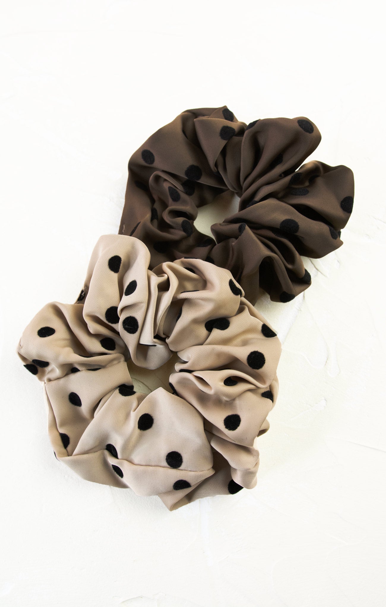 Two polka dot scrunchies, one brown and one beige, on a white background.