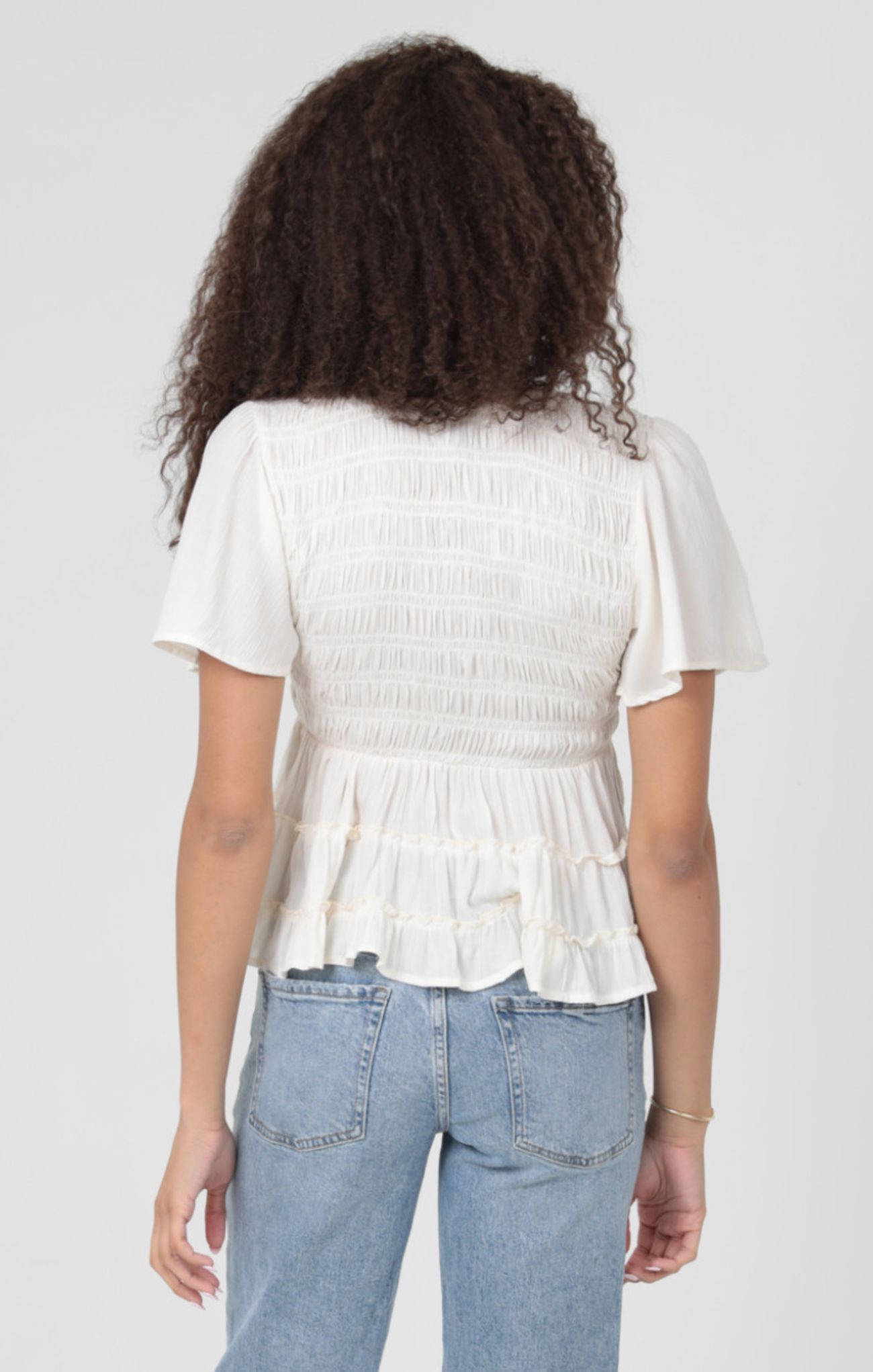 Person wearing a white ruffled blouse and blue jeans on a plain background