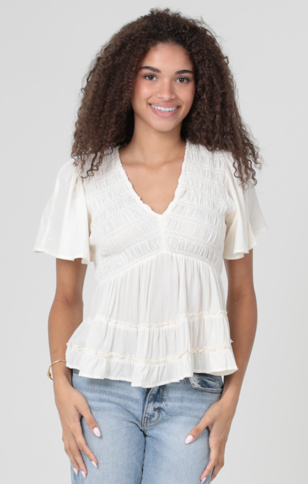 Woman wearing a white blouse and blue jeans against a plain background