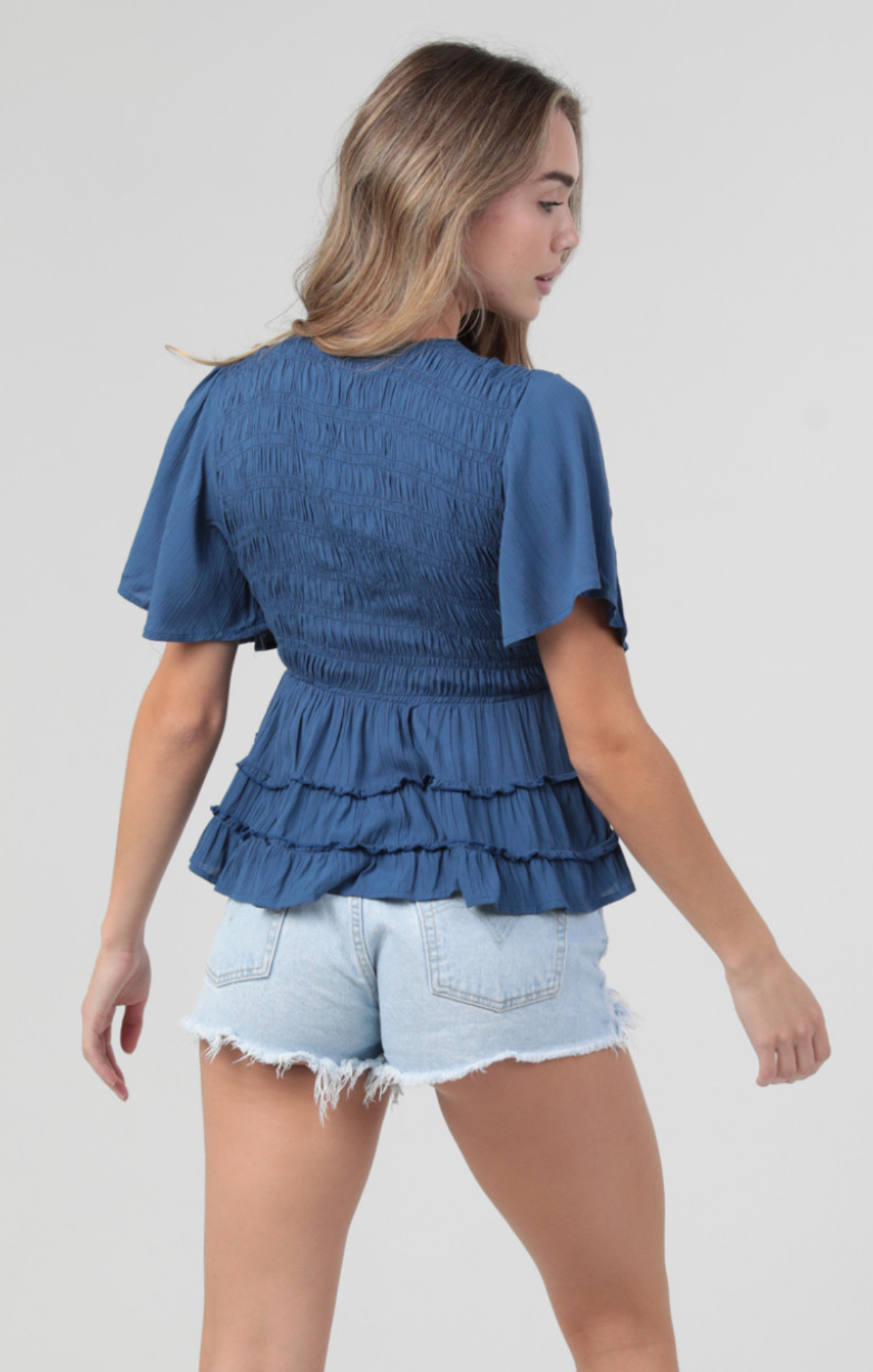 Woman wearing a blue ruffled top and denim shorts on a white background
