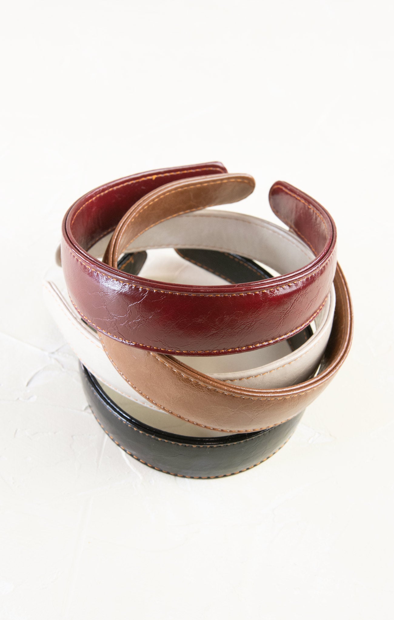 Stack of leather belts in various colors on a white background
