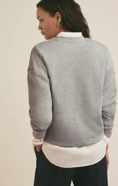 Person wearing a gray sweatshirt over a white shirt with a beige background