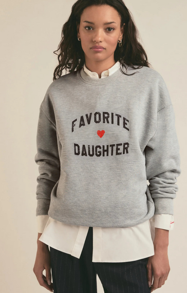 Person wearing a gray sweatshirt with 'Favorite Daughter' text and heart symbol on a plain background