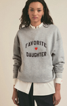 Person wearing a gray sweatshirt with 'Favorite Daughter' text and heart symbol on a plain background