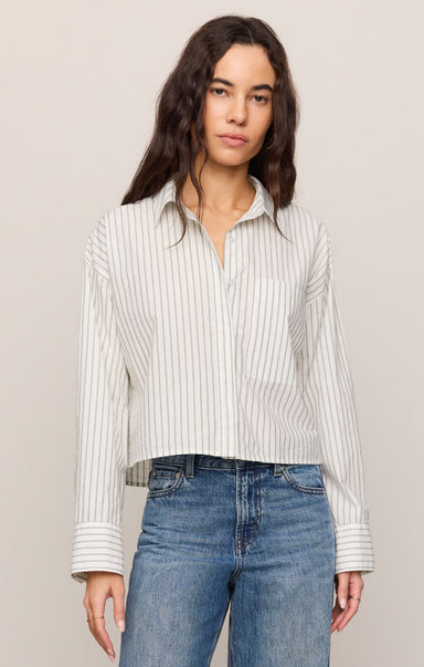 Woman wearing a striped shirt and blue jeans against a plain background