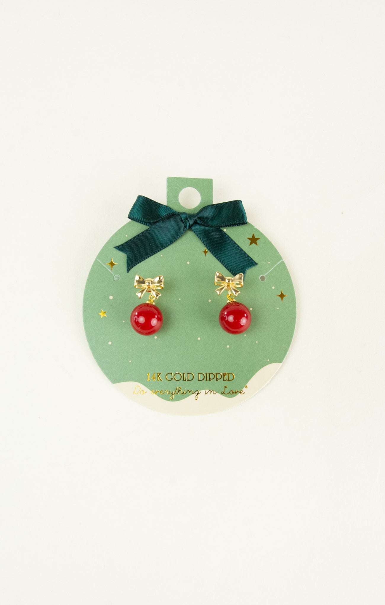 Pair of earrings with red balls and gold bows on a green card with a bow.