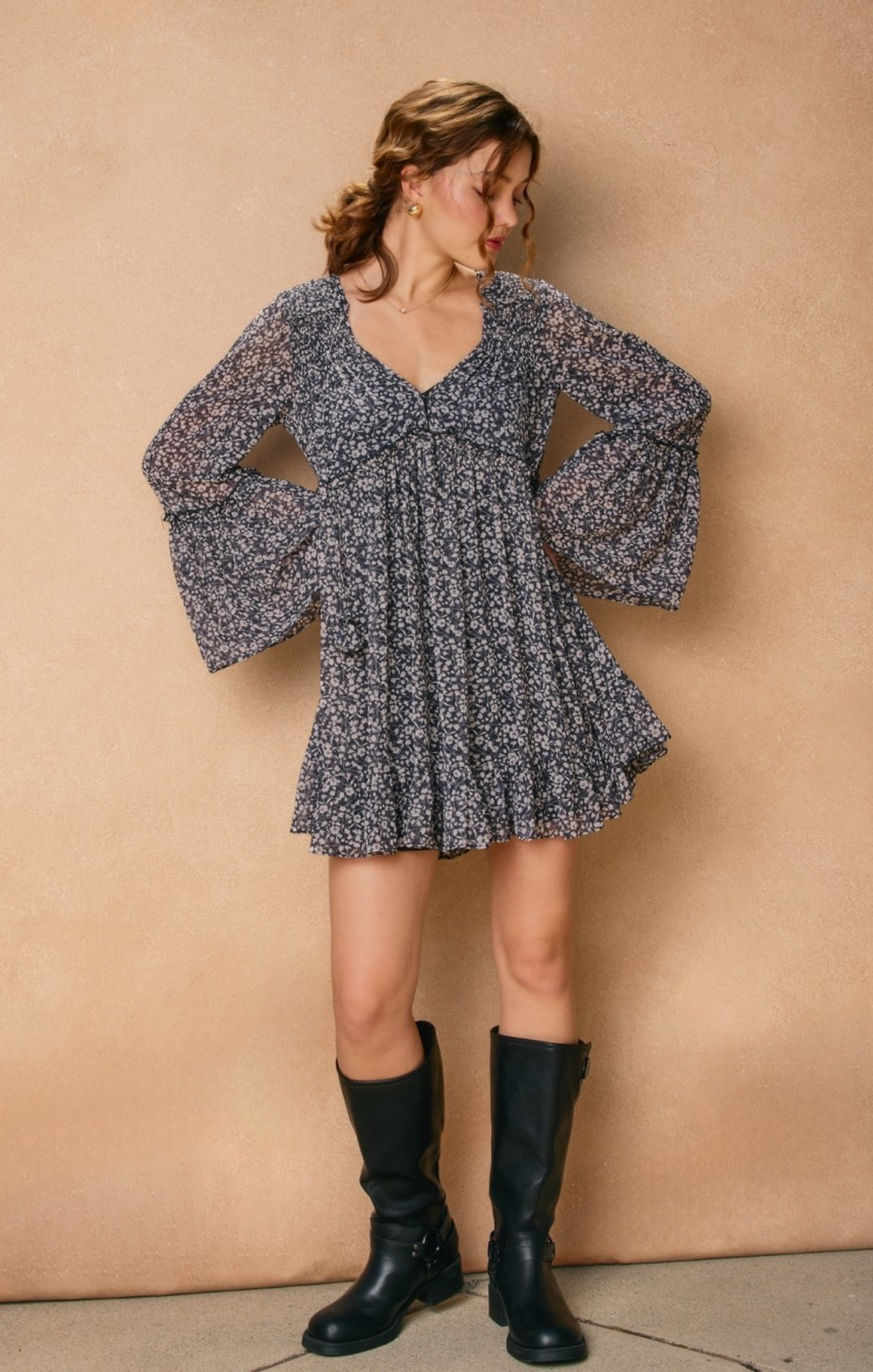 Woman wearing a floral dress with long sleeves and black boots against a beige wall.