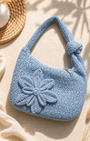 Blue crochet handbag with a flower detail on a beige surface
