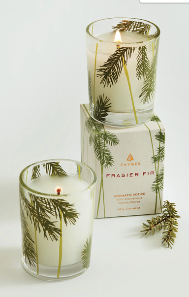 Two candles with pine tree design and packaging labeled 'Frasier Fir' on a white background.