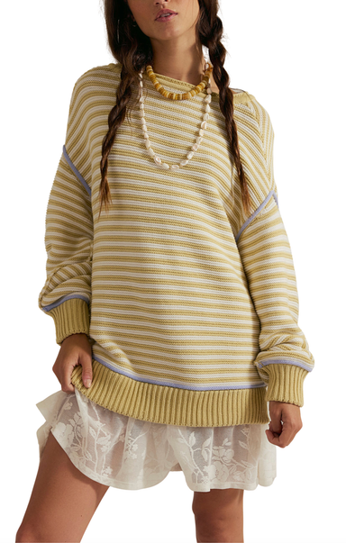 Woman wearing a yellow striped sweater with a white lace dress underneath on a white background