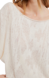 Close-up of a person wearing a textured beige top with a blurred background
