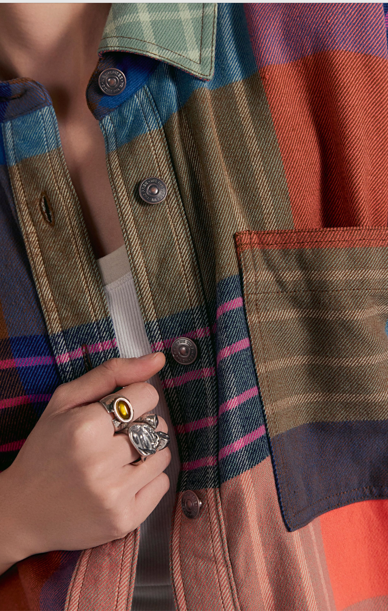 Person wearing a plaid jacket with a hand holding a ring featuring a yellow gemstone.