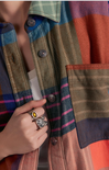 Person wearing a plaid jacket with a hand holding a ring featuring a yellow gemstone.