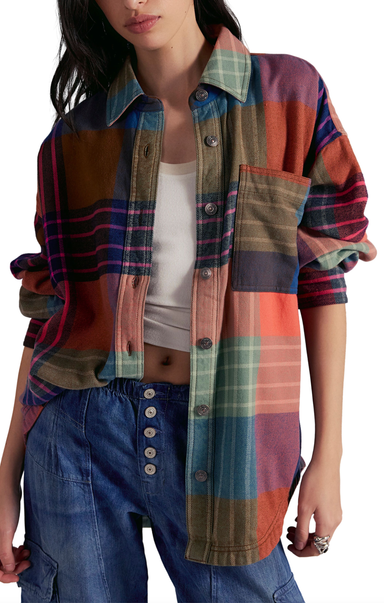 Person wearing a colorful plaid shirt over a white top and blue jeans on a white background