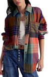Person wearing a colorful plaid shirt over a white top and blue jeans on a white background