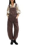 Person wearing brown overalls with a white shirt underneath on a white background
