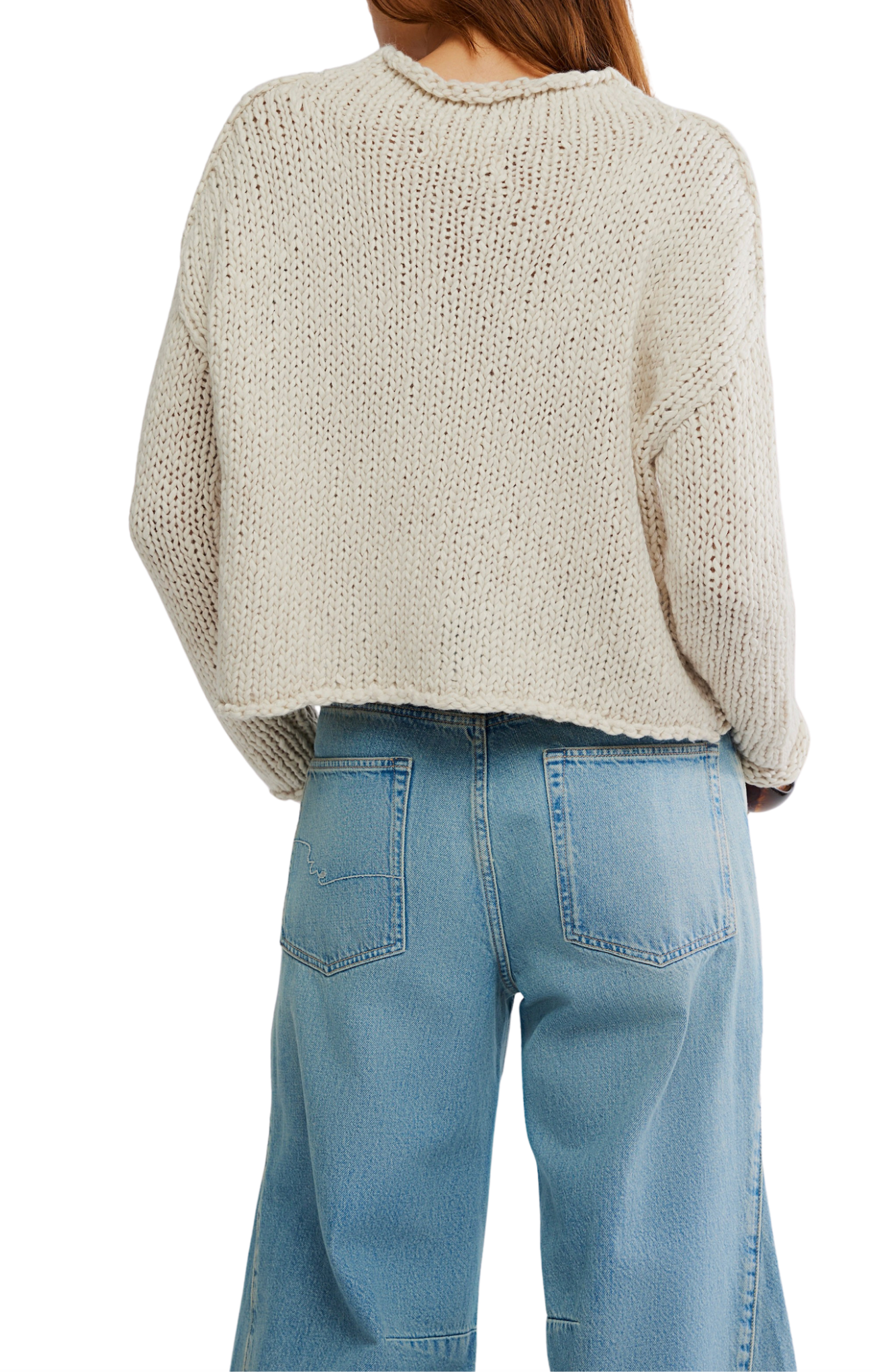Person wearing a beige knitted sweater and light blue jeans on a white background