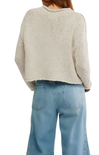 Person wearing a beige knitted sweater and light blue jeans on a white background