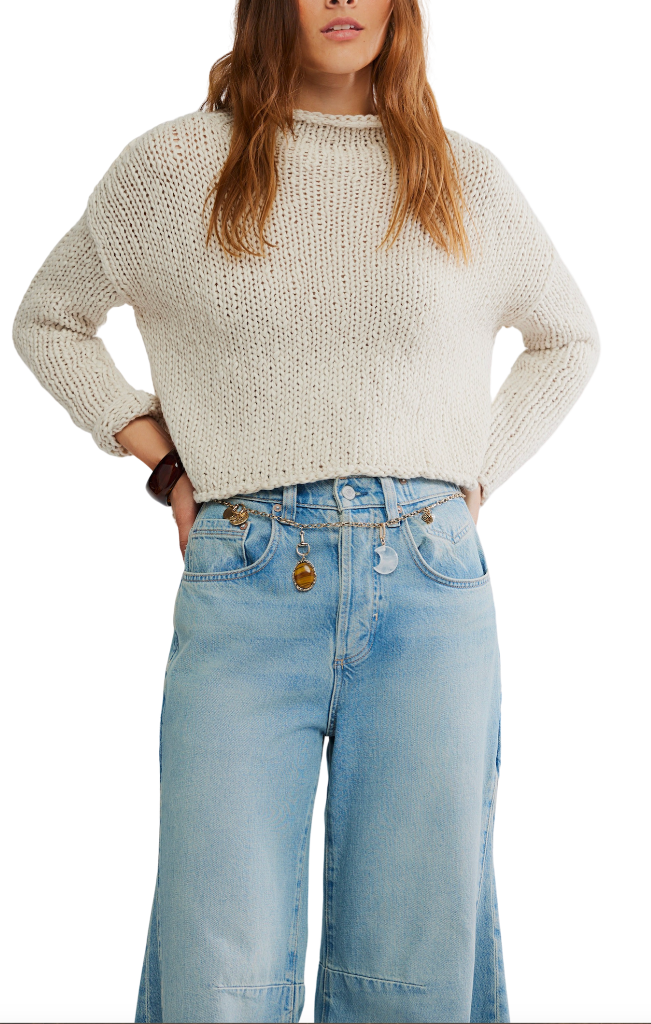 Person wearing a beige knitted sweater and light blue jeans on a white background