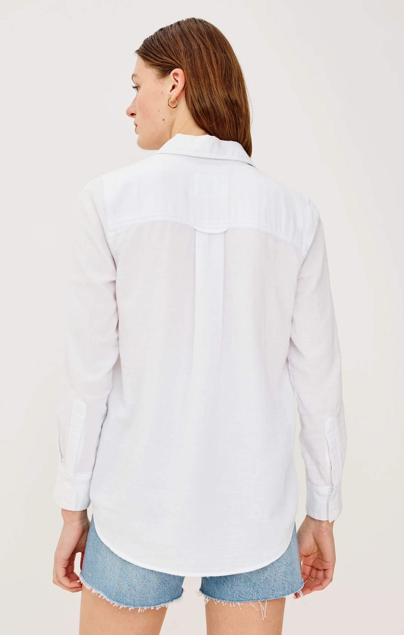 Woman wearing a white button-up shirt and denim shorts on a plain background