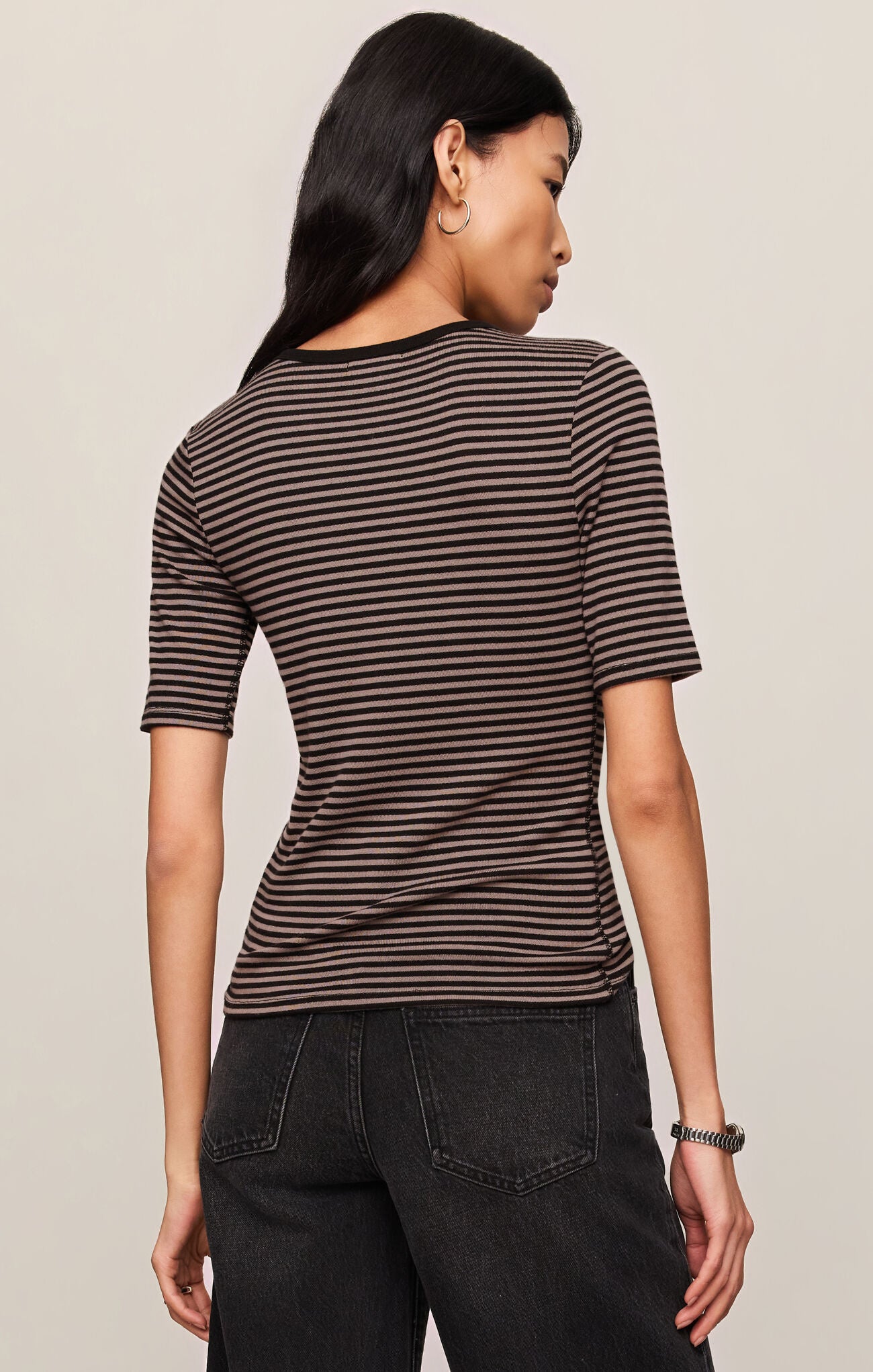 Woman wearing a striped shirt and black pants against a beige background