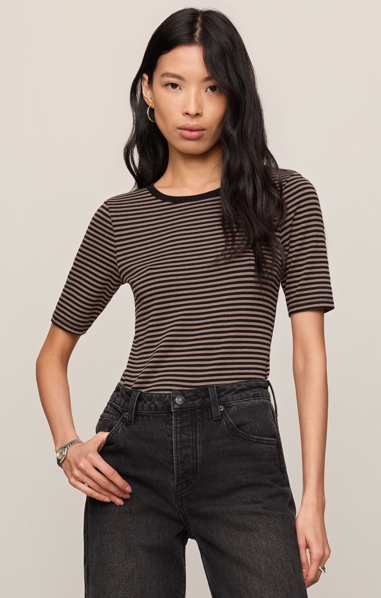 Woman wearing a striped shirt and black pants against a plain background