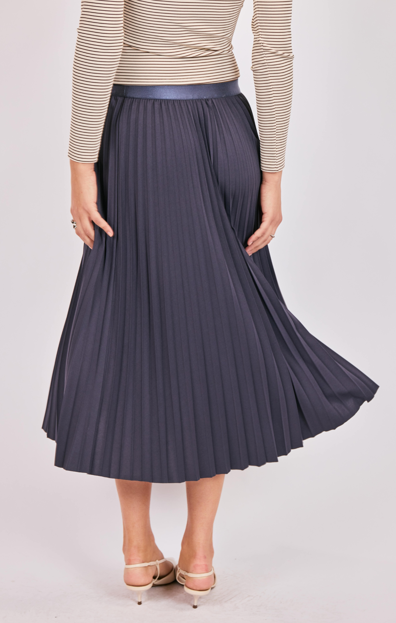 Person wearing a pleated navy skirt with a beige sweater on a light background