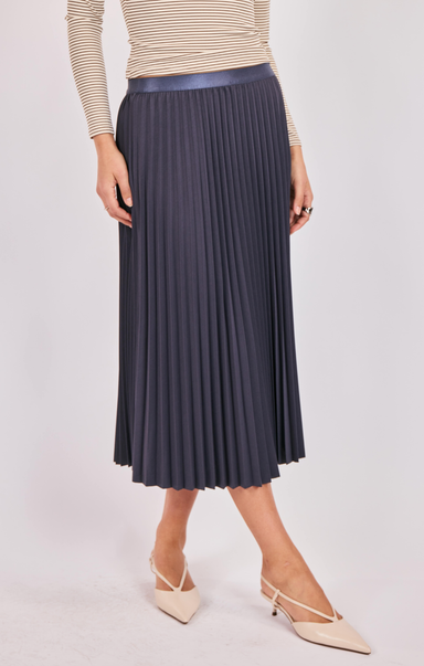 Person wearing a pleated navy skirt with a beige top and shoes on a light gray background