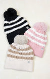 Three knit hats with pom-poms in black, pink, and beige on a white background