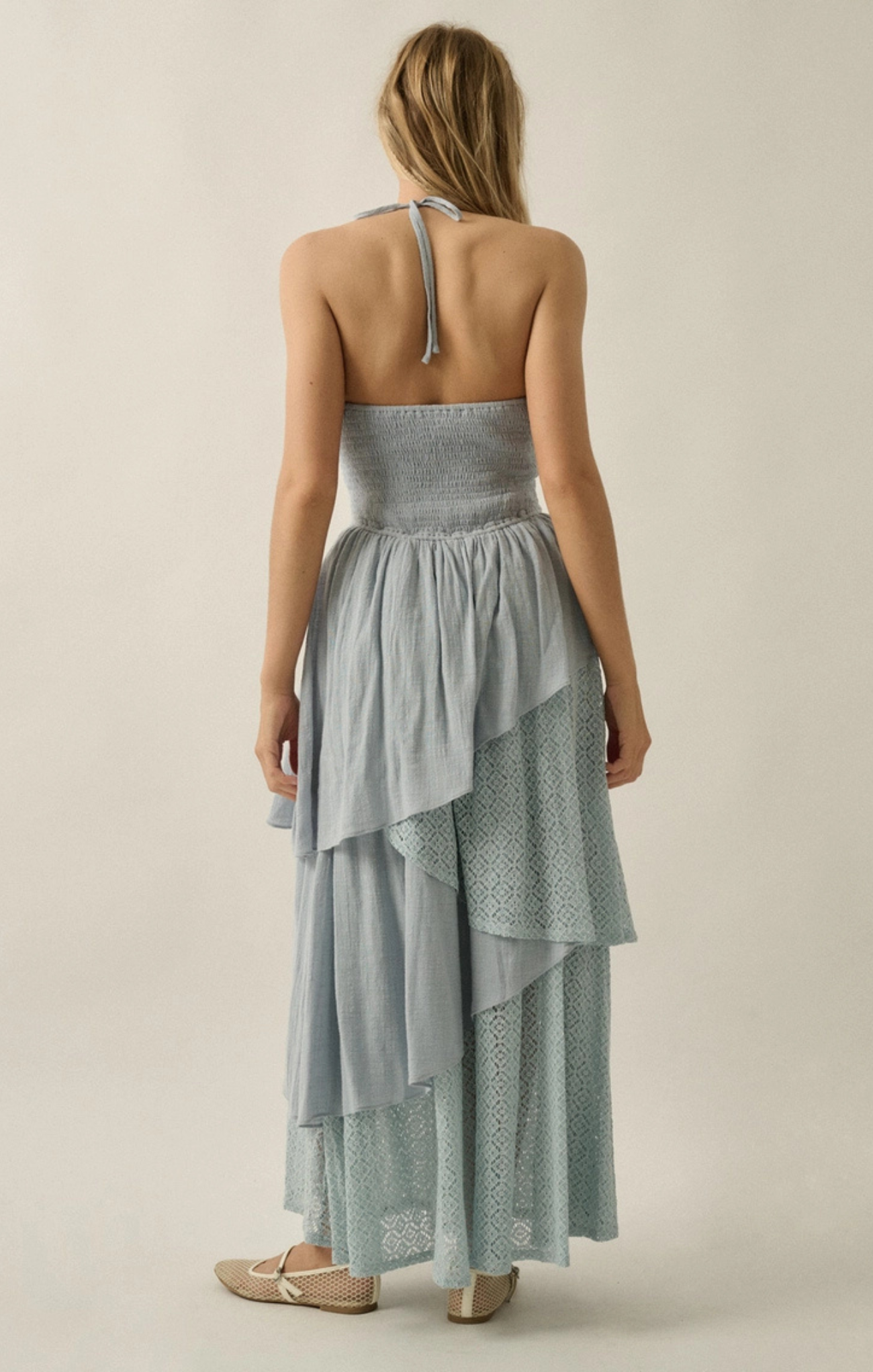 Woman wearing a light blue strapless dress with ruffled layers on a beige background