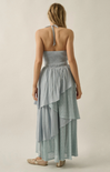 Woman wearing a light blue strapless dress with ruffled layers on a beige background