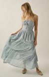 Woman wearing a light blue strapless dress with a textured pattern on a plain background