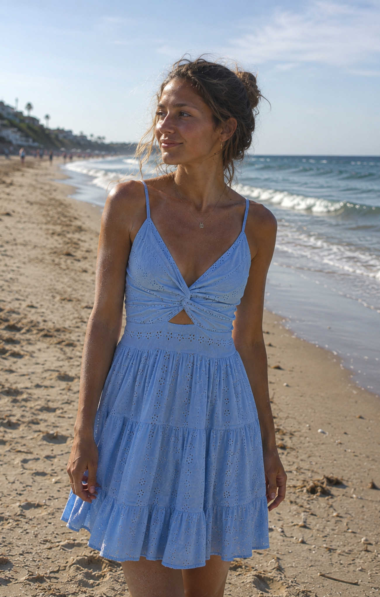 Woman in a light blue dress standing on a beach with ocean waves in the background